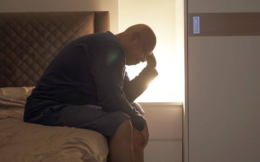 Man sitting on the edge of his bed unable to sleep